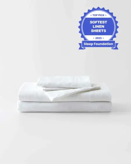 Luxurious white linen sheets stacked on a bed, highlighting soft and breathable bedding options recommended for optimal sleep comfort.