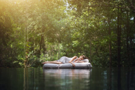 Cloud floating bed on water with lush forest background, serene natural sleep environment, eco-friendly mattress, and sustainable bedding, promoting restful sleep and relaxation in nature, The Mattress Underground SEO image.